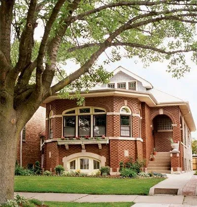 A bungalow house design with a nice lawn and stairways that lead to the main entrance of the house. 