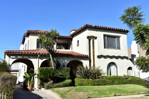 A typical Spanish bungalow house design with white outer walls, lots of arches, and a good amount of greenery. 