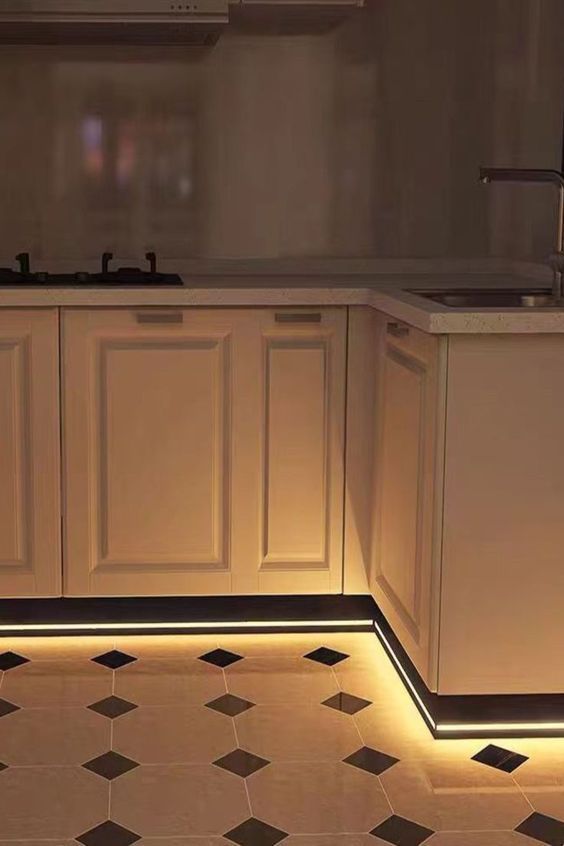 A kitchen with profile lights affixed to the cabinet to illuminate the floor