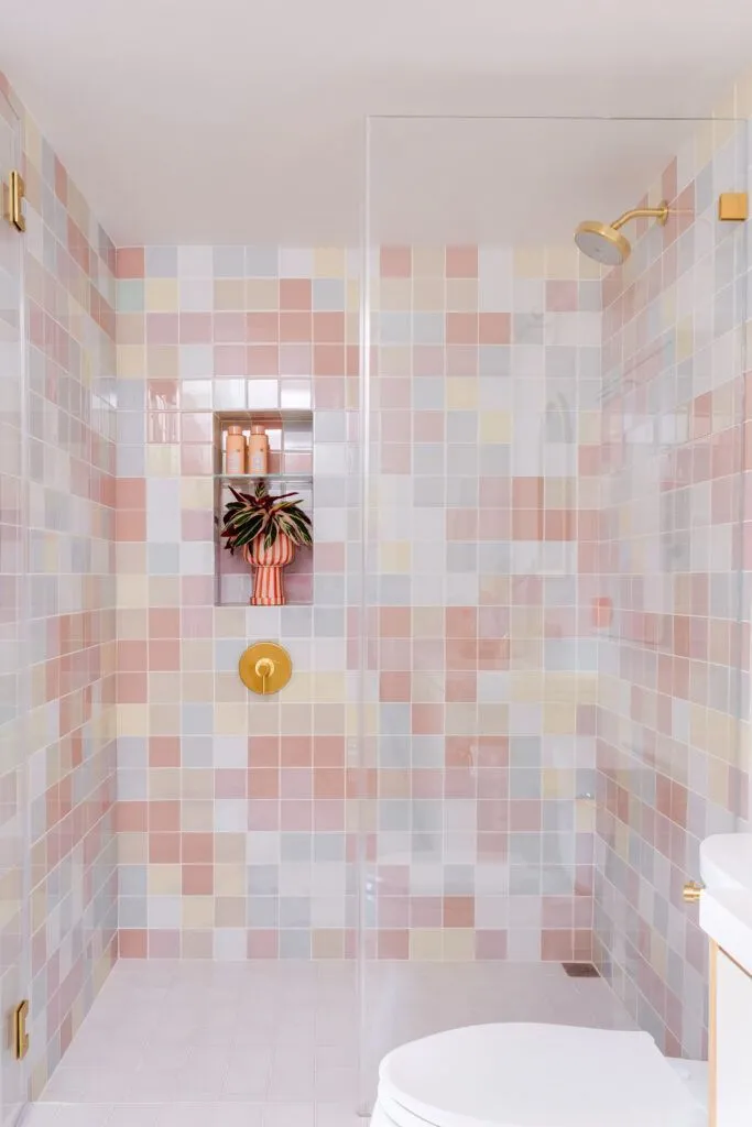 Square pastel tiles in shades of pink, peach, blue, and yellow on shower walls against white floor tiles