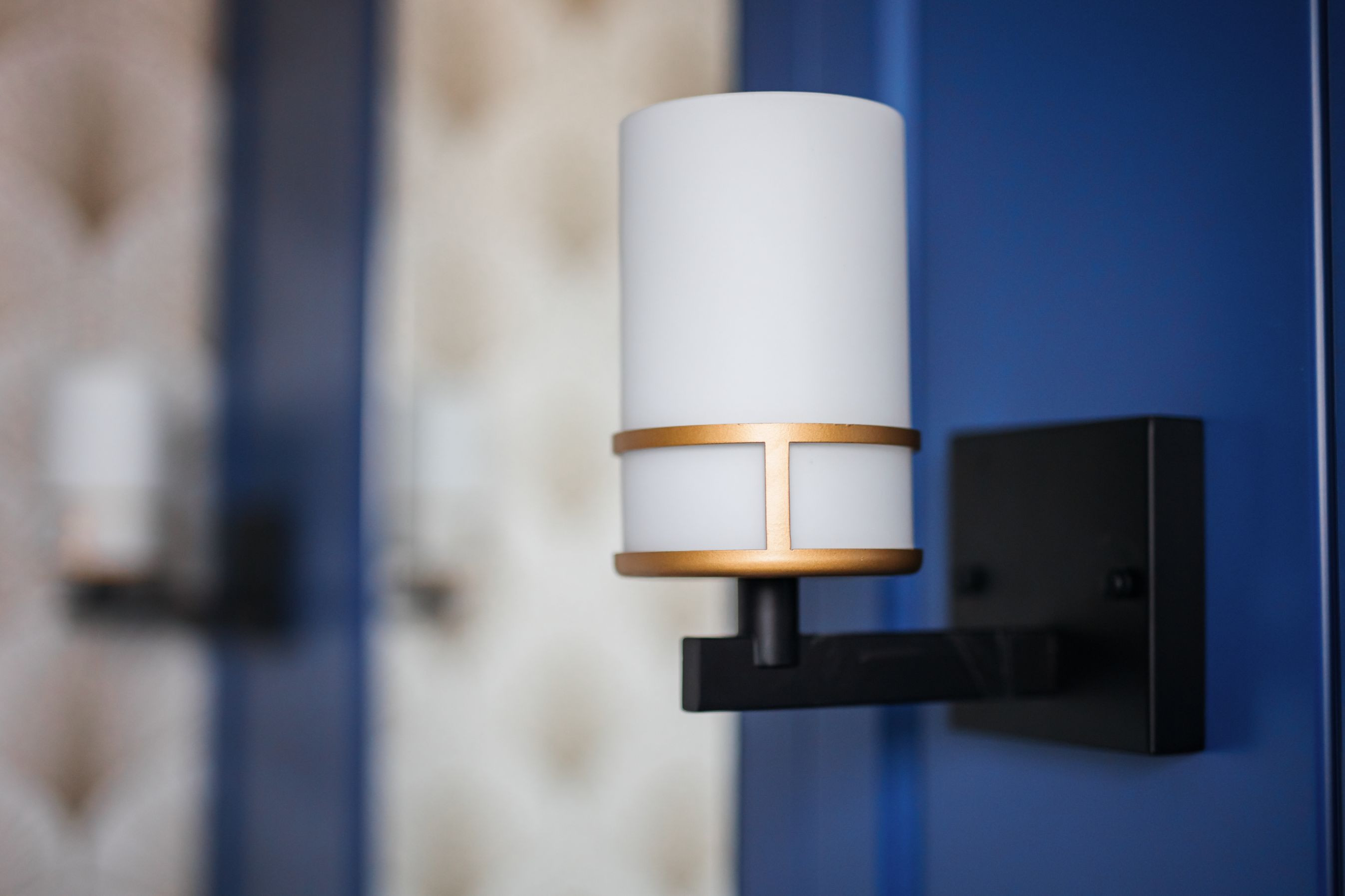 A cylindrical modern wall light mounted on a blue wall